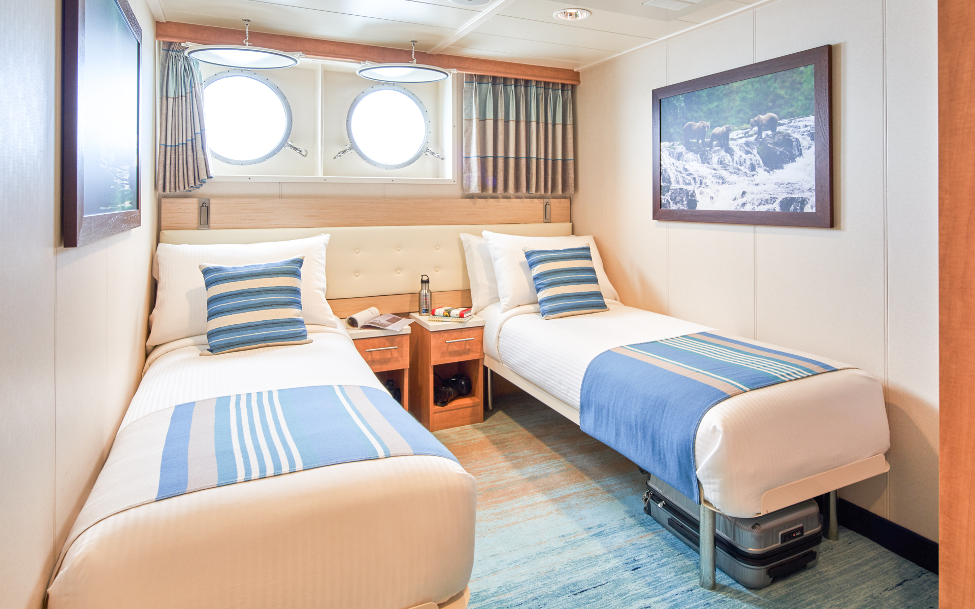 Twin beds with nightstands in between and two portholes in Cat 1 cabin aboard National Geographic Venture expedition ship
