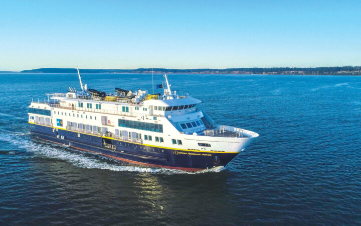 Exterior shot of National Geographic Venture ship in the open sea. Her blue hull coasts on calm waters in the morning sunlight