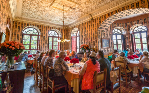 Ecuador's Andes Highland Haciendas travelers sit at a luncheon at a rose plantation in an ornate room with high ceilings.
