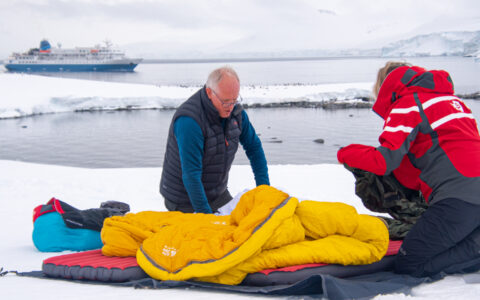 Antarctic campers roll up their gear from the night prior on the snow and ice next to the the water where their small cruise ship is parked