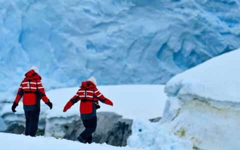 Hikers in winter gear and red adventure jackets walk down as they navigate the glaciers and snow