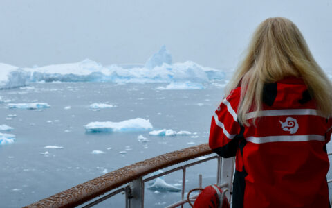 Women looks off into the distance off small cruise ship into icy landscape and broken up iceberg