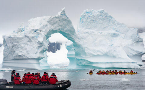 Guests exploring Antarctica next to a breathtaking iceberg in a zodiac and a group of kayakers on a cloudy day