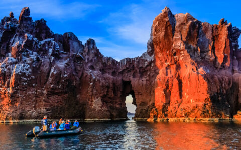 Black Zodiac boat with Baja California Discovery cruise guests drifts beside eroded white & white canyon walls at sunset.