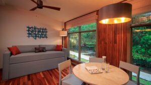 Suite living room at Hotel Senda Monteverde, with small table, gray chairs & couch, modern design, wood accents & large view windows.