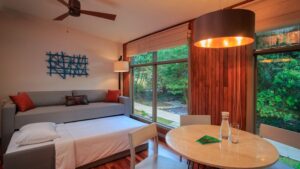 Suite living room at Hotel Senda Monteverde, with small table, gray chairs & couch pulled out, modern design, wood accents & large view windows.