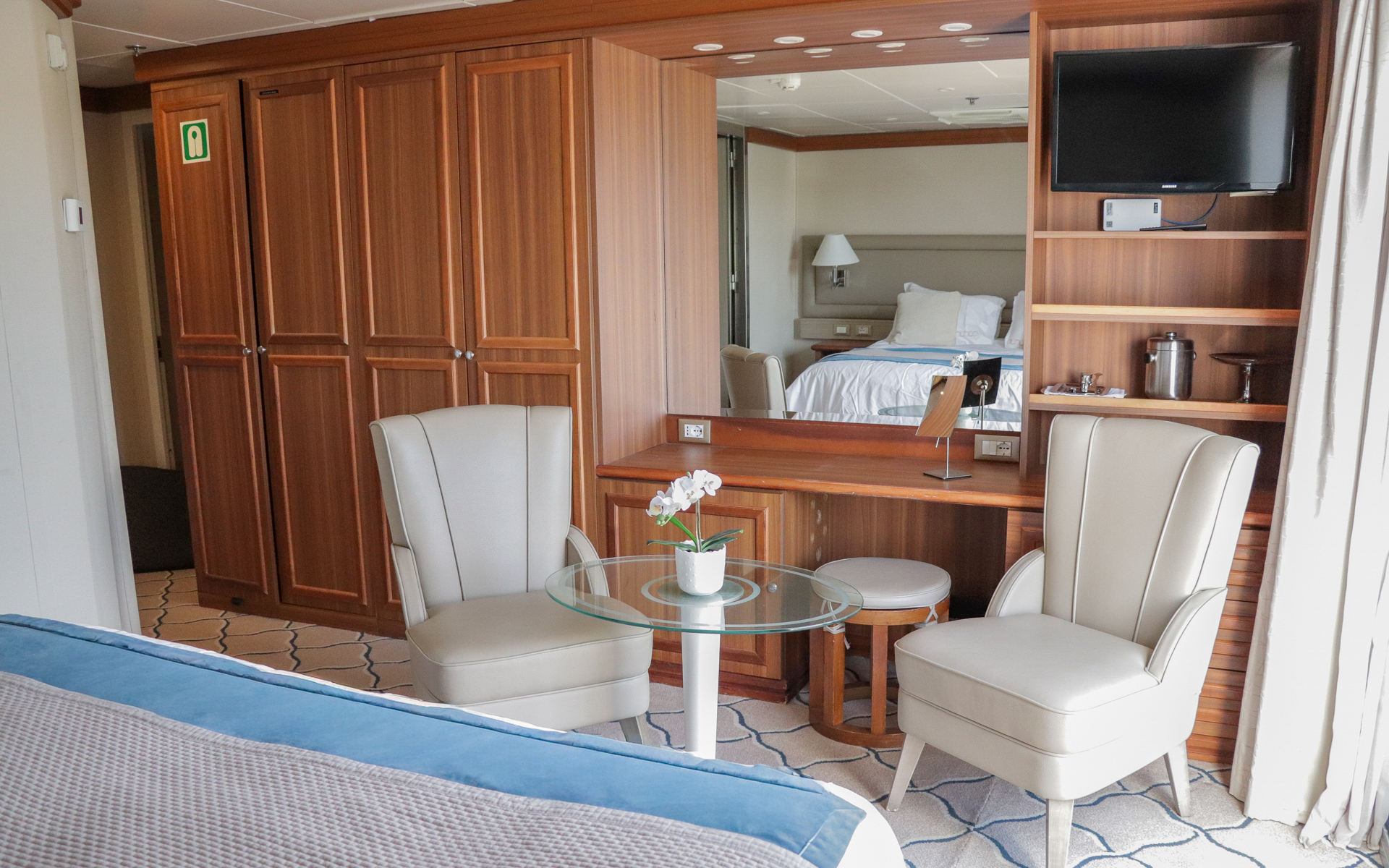 Navigator Stateroom aboard Discoverer: Polar Latitudes boasts large bed fitted with white & tan linens next to multiple storage compartments and seating at its foot.