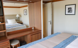 Owner's Suite aboard Discoverer: Polar Latitudes with large mirror, stool, storage and large bed with white linens.
