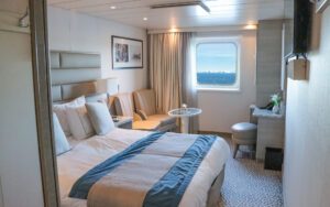 Solo Vista Stateroom cabin aboard Discoverer: Polar Latitudes with large viewing window, chairs & small table next to a bed fitted in white and tan linens.