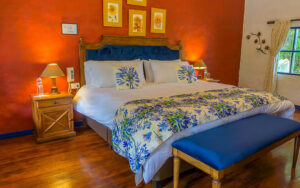 Wooden double bed with bench in floral sheets at Hacienda Pinsaqui with wood floors, window & red & white walls.