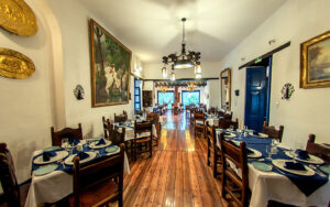 Dining room at Hacienda Pinsaqui with traditional wooden tables set for dinner, white adobe walls & gold-accented artwork.