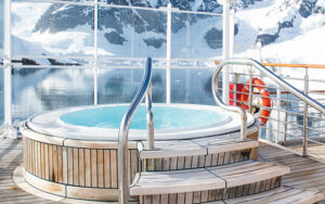 Open-air Jacuzzi wrapped in wooden planks with view of polar landscape in the background through large wind-blocking windows.
