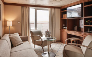 Living room area with couch, two arm chairs, small table and television in Owner's Suite on small ship Heritage Discoverer.
