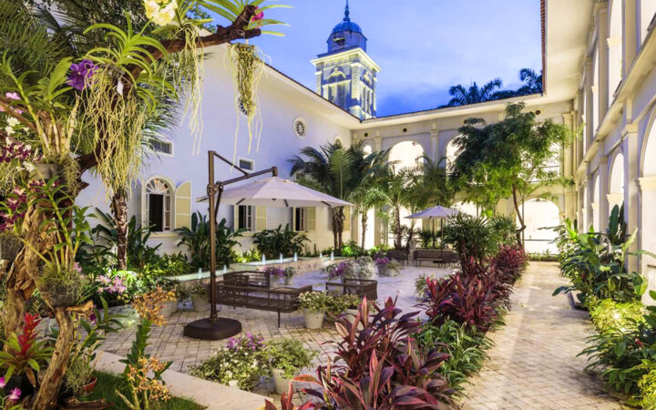 Courtyard of luxury Hotel del Parque in Guayaquil, Ecuador, with lush plants in bloom, stone floor & view to belltower.