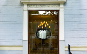 Hotel entrance with it's name, "Hotel del Parque" written above the 2 glass doors. A baby blue wall and white trim outline the door.