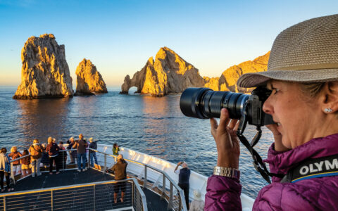 Guests gather on the bow of the ship National Geographic Venture and photograph the sunrise at Lands End, Cabo San Lucas, Baja California, Mexico