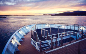 Orange and purple tones illuminate the sky during sunset, seen from the bow of National Geographic Quest expedition ship