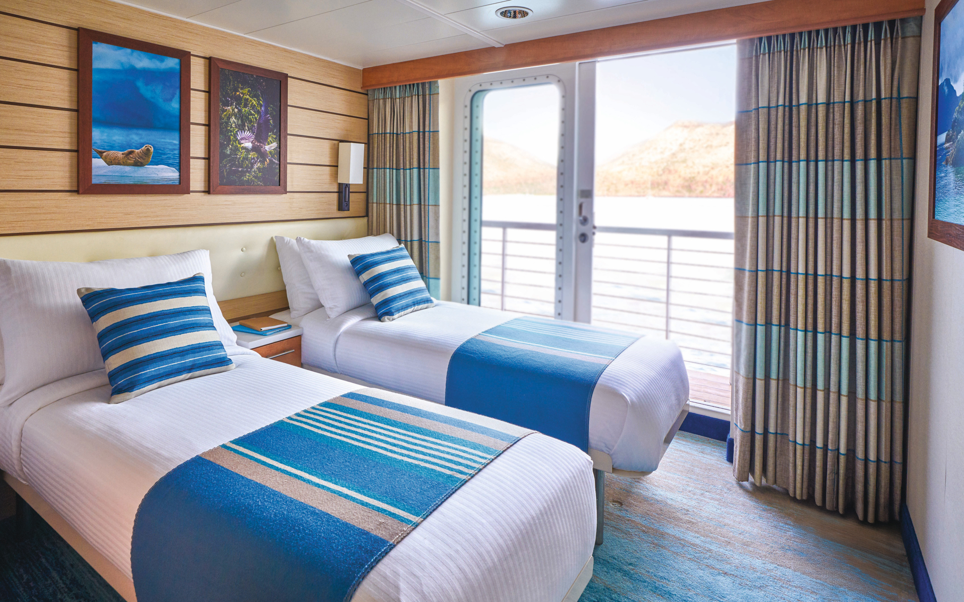 National Geographic Quest category 4 suite with two twin beds wrapped in white linens next to glass door for patio access.