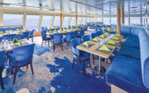 Spacious dining room with elegant table setting, royal blue seating and window-lined walls aboard National Geographic Quest expedition ship