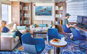 Library with couches, tables, chairs, book cases, desk with computers and TV aboard National Geographic Quest expedition ship