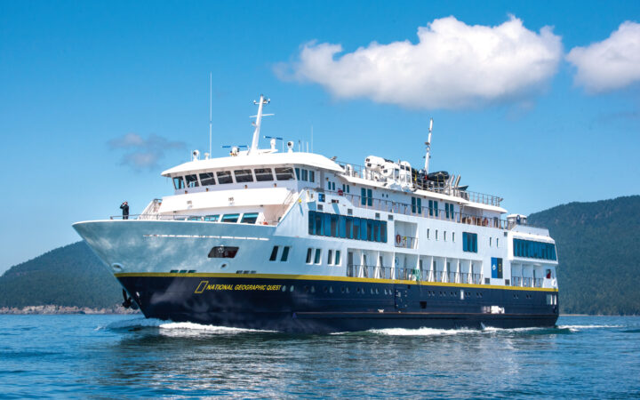 Full exterior of port side and dark blue bow of National Geographic Quest expedition ship sailing calm waters on a clear day
