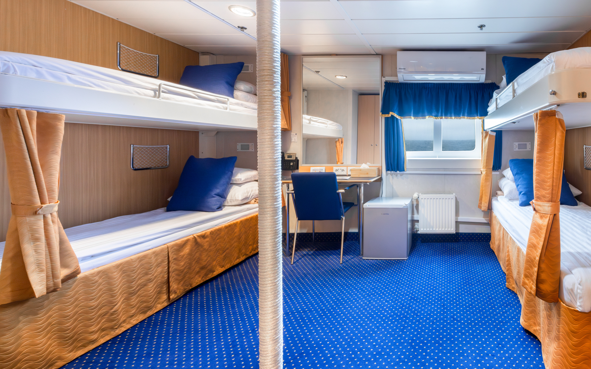 2 lower & 2 upper twin beds in white linens in quad cabin with blue & gold accents, small desk & armoire on Ocean Nova ship.