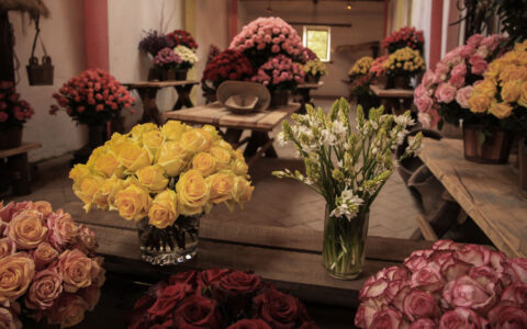 Jars of roses in yellow, pink & burgundy sit on wooden tables in a hacienda, seen on the Otavalo Escape tour in Ecuador.