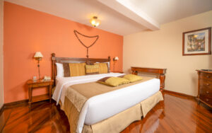 King bed with white linens in front of terracotta colored wall on lower floor of Duplex Twin Room King at Hotel Patio Andaluz.