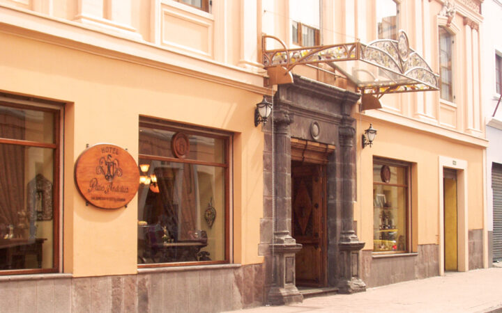 Doorway to Hotel Patio Andaluz stands out on a yellow building in Ecuador. Wooden sign and elegant dark stone marks the entrance