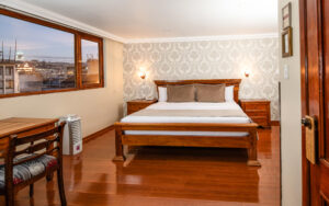 4th floor Superior Premium Room at Hotel Patio Andaluz with a view of Quito from large corner windows. Desk and 2 nightstands near bed.