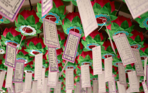 Paper tags with Japanese symbols hang from red, green & teal fabric flowers in a cluster on a Japan circumnavigation cruise.