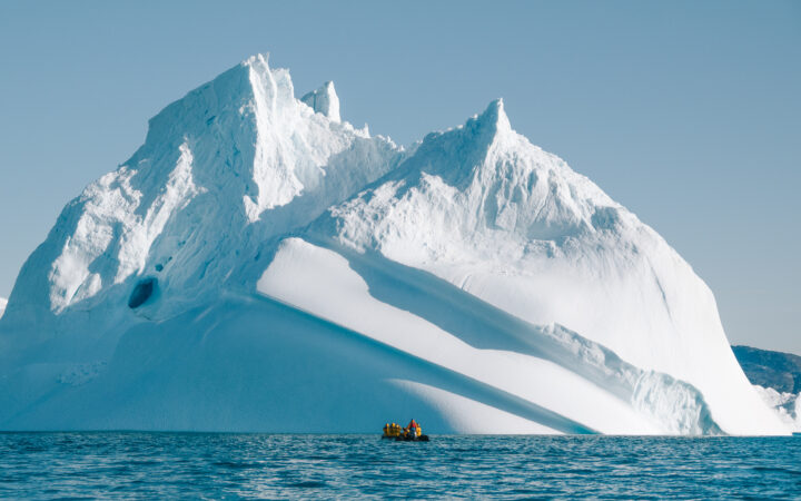 Zodiak next to towering iceberg in Ilulissat Icefjord, a UNESCO World Heritage Site during Southeast to West Greenland cruise