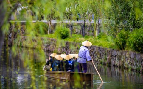 Springtime Splendor cruise guests enjoy a canal boat ride while wearing conical hats & being poled along among willow trees.