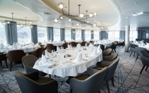 Dining room with modern decor, large tables in white tablecloths & fine dinnerware aboard Ultramarine small expedition ship.