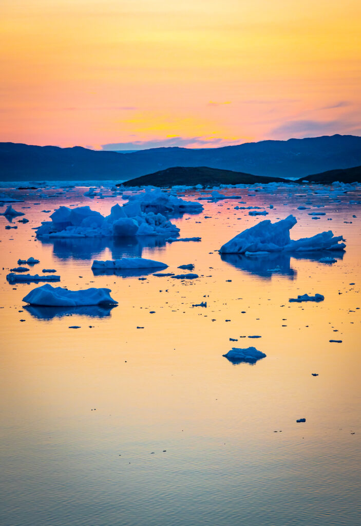 A sunset in Antarctica with orange sky and blue icebergs