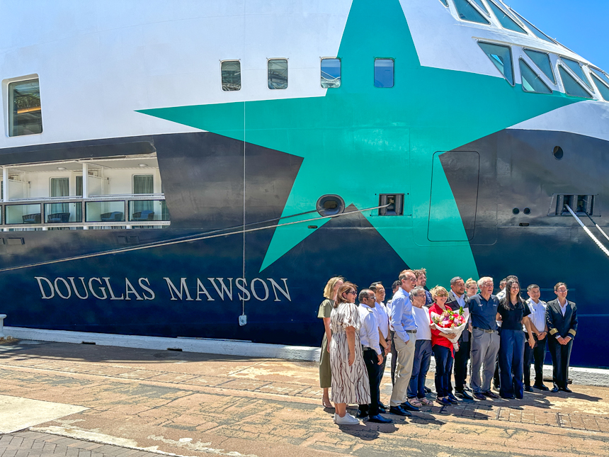 Christening of Douglas Mawson with guests posing for photo in front of new ship with bright green star on the side of the ship