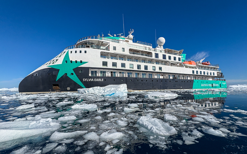 Expedition ship with white and blue design, Sylvia Earle cruising through the icebergs on a sunny bluebird day in Antarctica