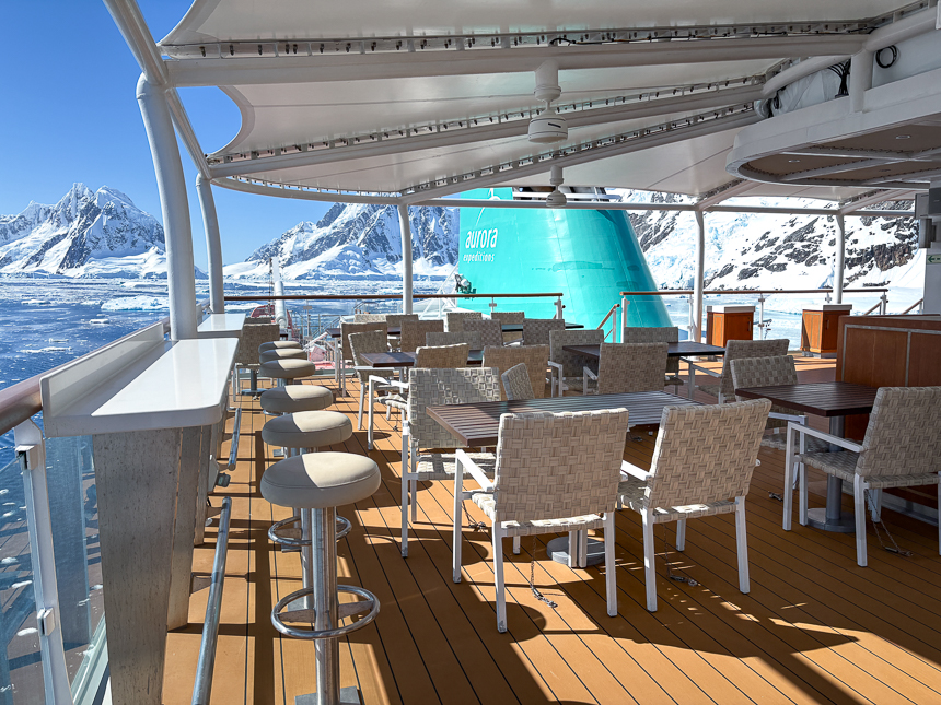 Deck with a seating area aboard the Sylvia Earle, small ship cruise on a sunny day in Antarctica with snowy mountains off in the distance 