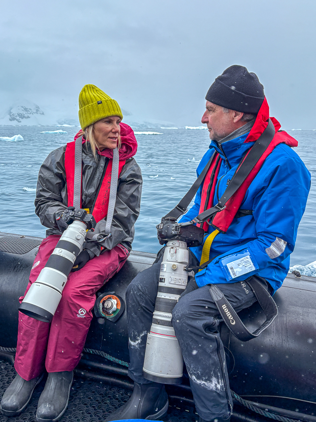 A man and woman facing each other on a Zodiac in Antarctica with large cameras in their hands