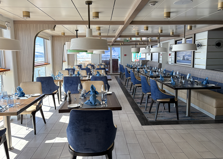 Restaurant aboard Sylvia Earle with blue velvet chairs, nice place settings, overhanging lights and large windows 