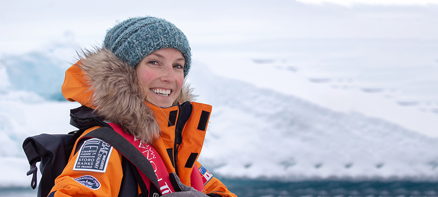 Women wearing parka and beanie posing in front of iceberg on a bright sunny day off a small ship cruise
