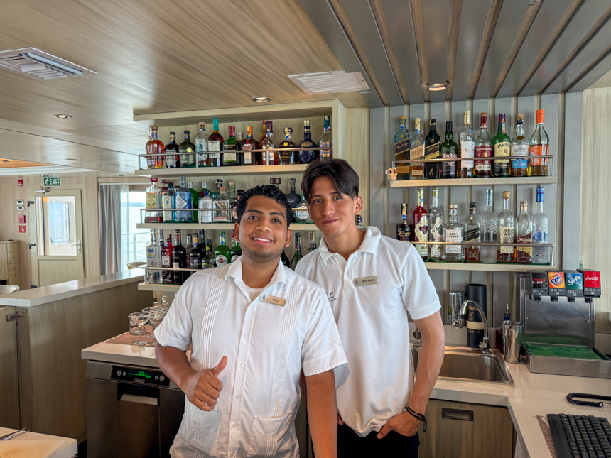 two Bartenders dressed in white shirts smiling in front of full stocked bar