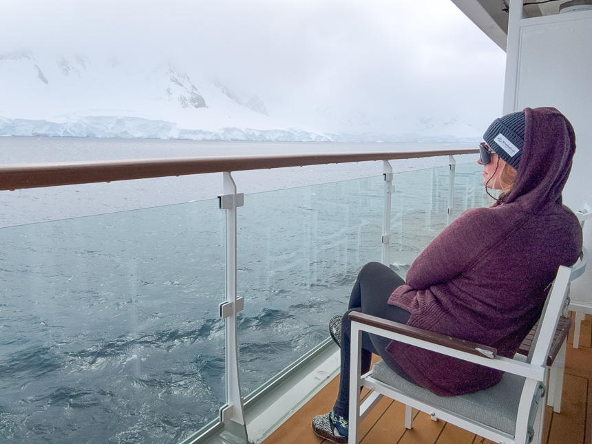 AdventureSmith Jenn sitting in a chair enjoying her balcony aboard Sylvia Earle on a cloudy day off the coast of Antarctica