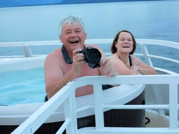 Happy guests in the hot tub on their small ship cruise in Alaska taking pictures of the scenery as they sail.