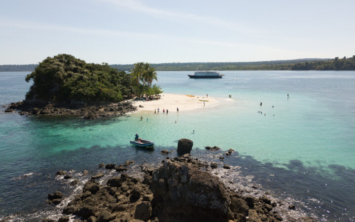 Small-ship expedition cruise Safari Voyager anchored off a sandy islet in Panama, with guests kayaking, paddleboarding, and swimming in turquoise water.