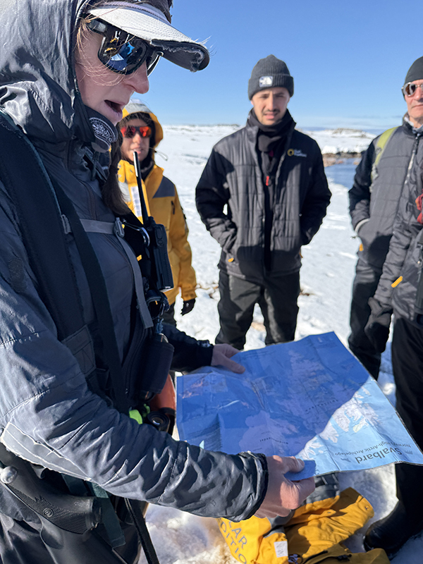 A guide holds a map of Svalbard with travelers in a circle around her