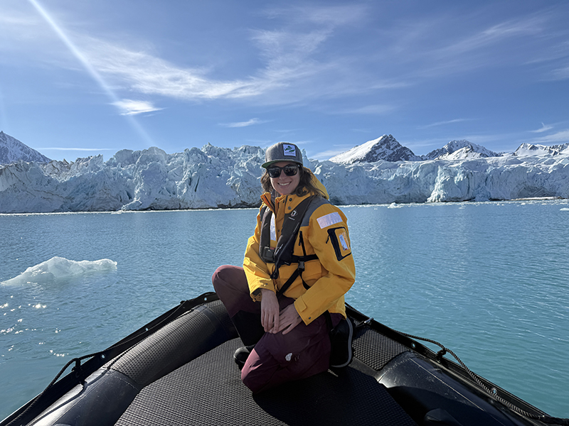 AdventureSmith specialist Taylor poses on the bow of a Zodiac in Svalbard wearing a yellow jacket
