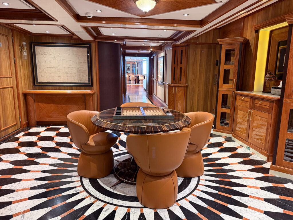 Inside Aqua Lares, rich wooden walls and black and white rich marble floor, a circular table with backgammon board and four chairs. 