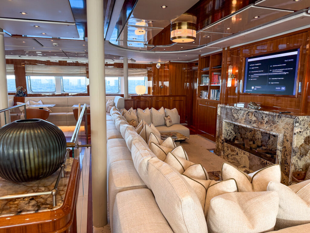 Salon aboard luxury yacht Aqua Lares, rich wood interior with marble fireplace and white couches and pillows. 