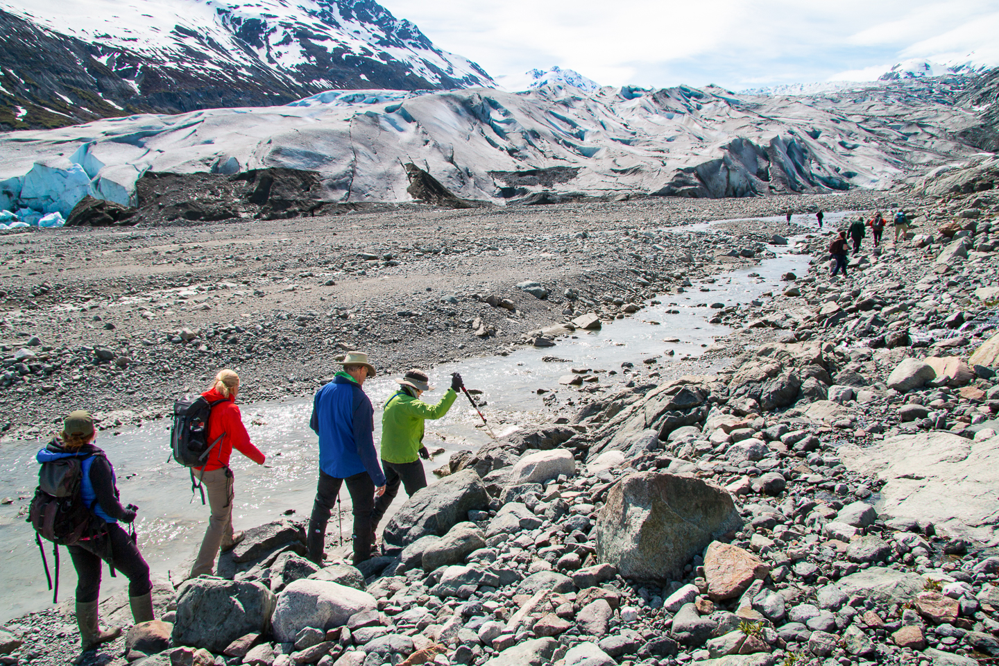 A group of travelers hike among rocks and streams as they approach the face of a glacier in Alaska, Glacier Bay National Park